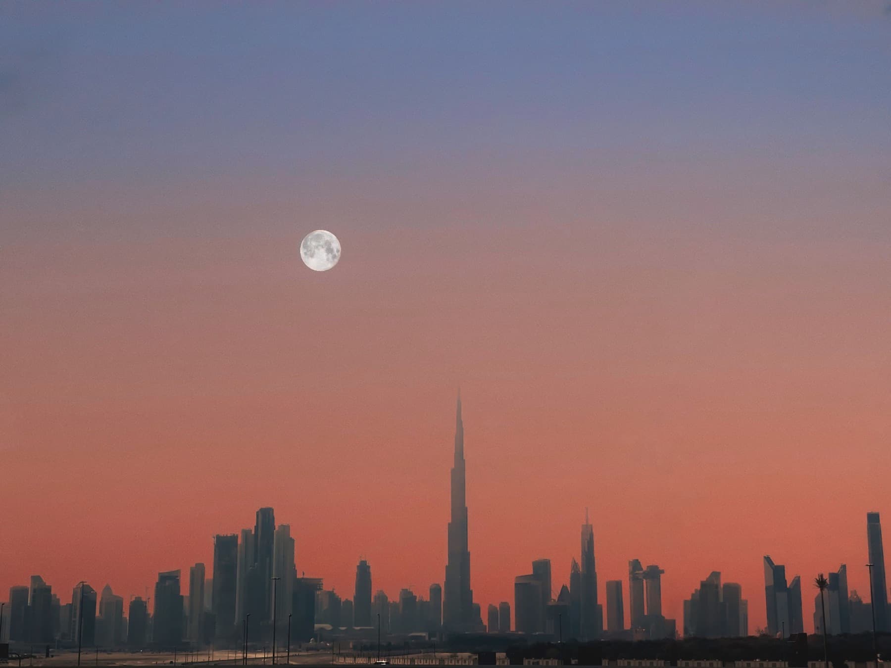 The Dubai skyline at dusk with a full moon over the Burj Khalifa