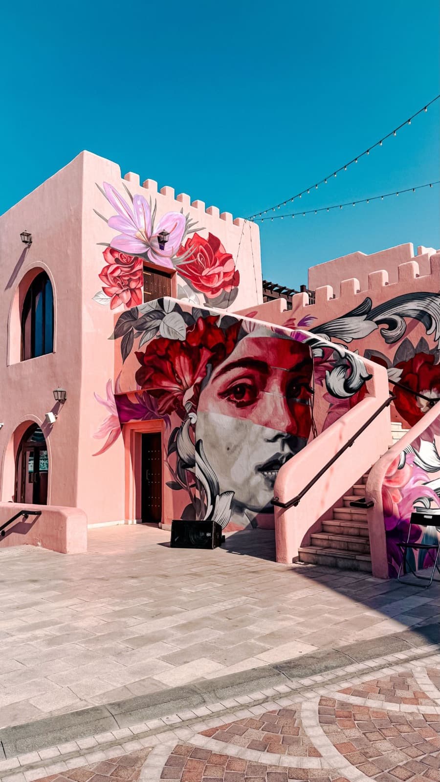 A pink building covered in a floral mural of a woman's face