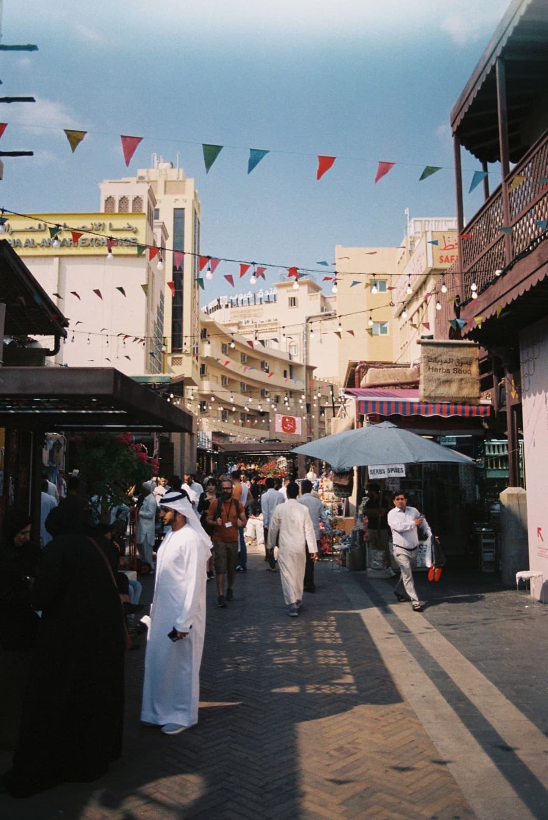 People walking through a busy souq street under bunting